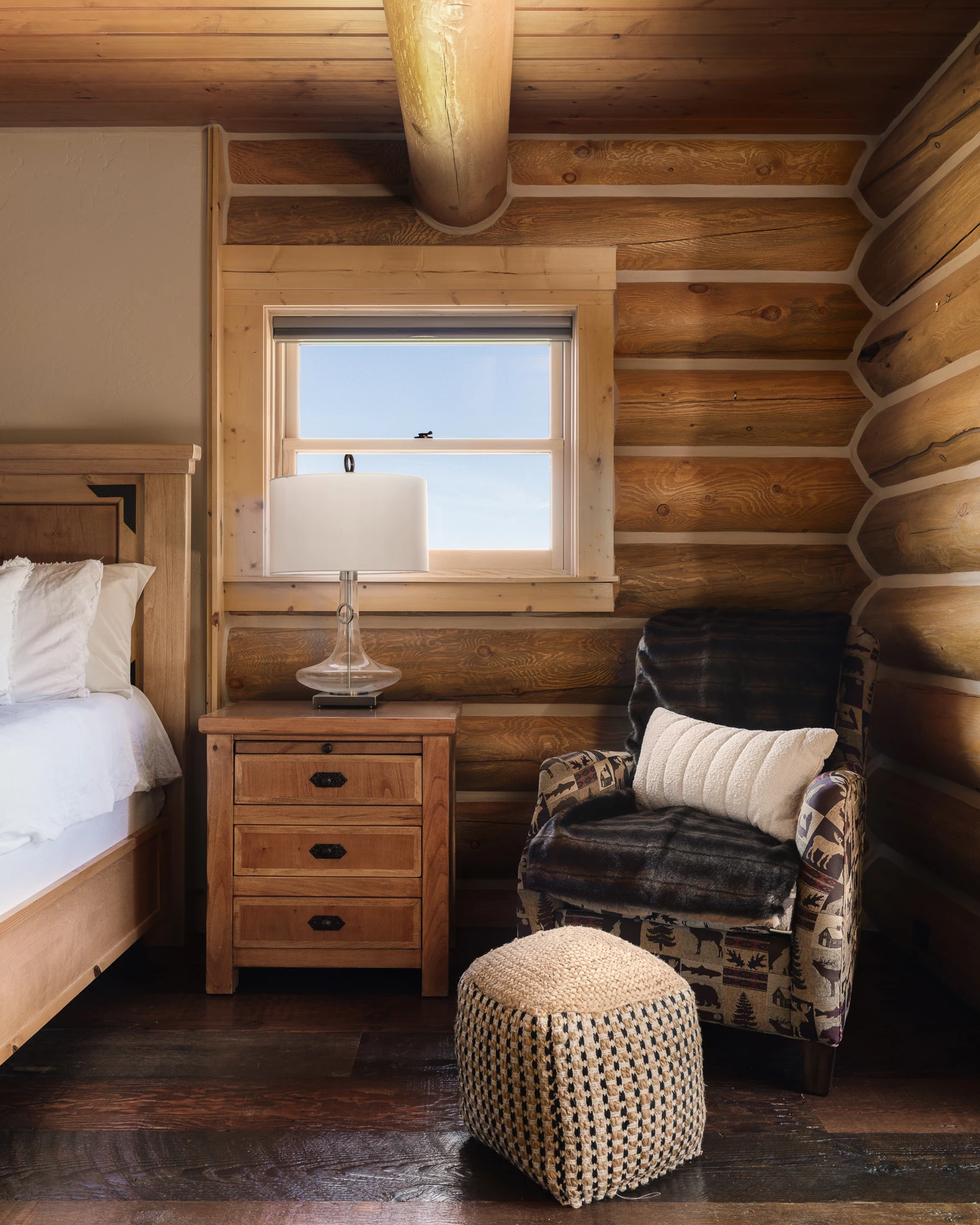 Bedroom nightstand and plaid armchair beneath a log-framed window — interior design photography Livingston Montana, Bear Canyon Ranch